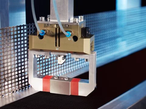 Ein Roboterarm greift Bauteile vom Förderband, um sie lagerichtig dem nächsten Fertigungsschritt zuzuführen. Die Ankunft des nächsten Bauteils signalisiert ihm ein Laser-Lichttaster mit Hintergrundausblendung der Subminiaturbaureihe FT 10, der dank seiner winzigen Abmessungen direkt im Robotergreifer montiert werden kann.